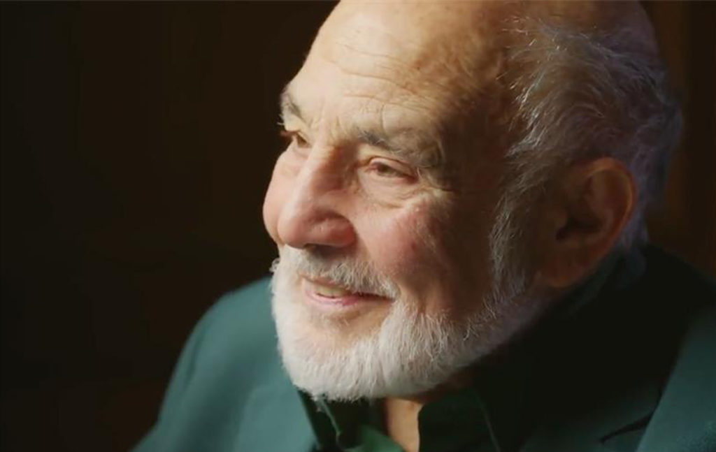 a man with a white beard wearing a green shirt smiling